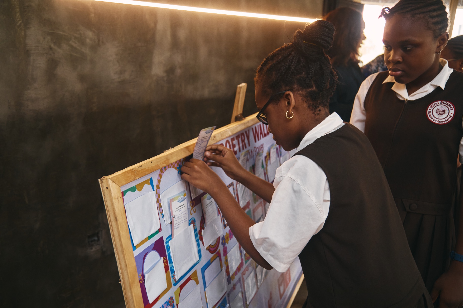 Child pinning her handwritten poem to a Poetry Wall display board